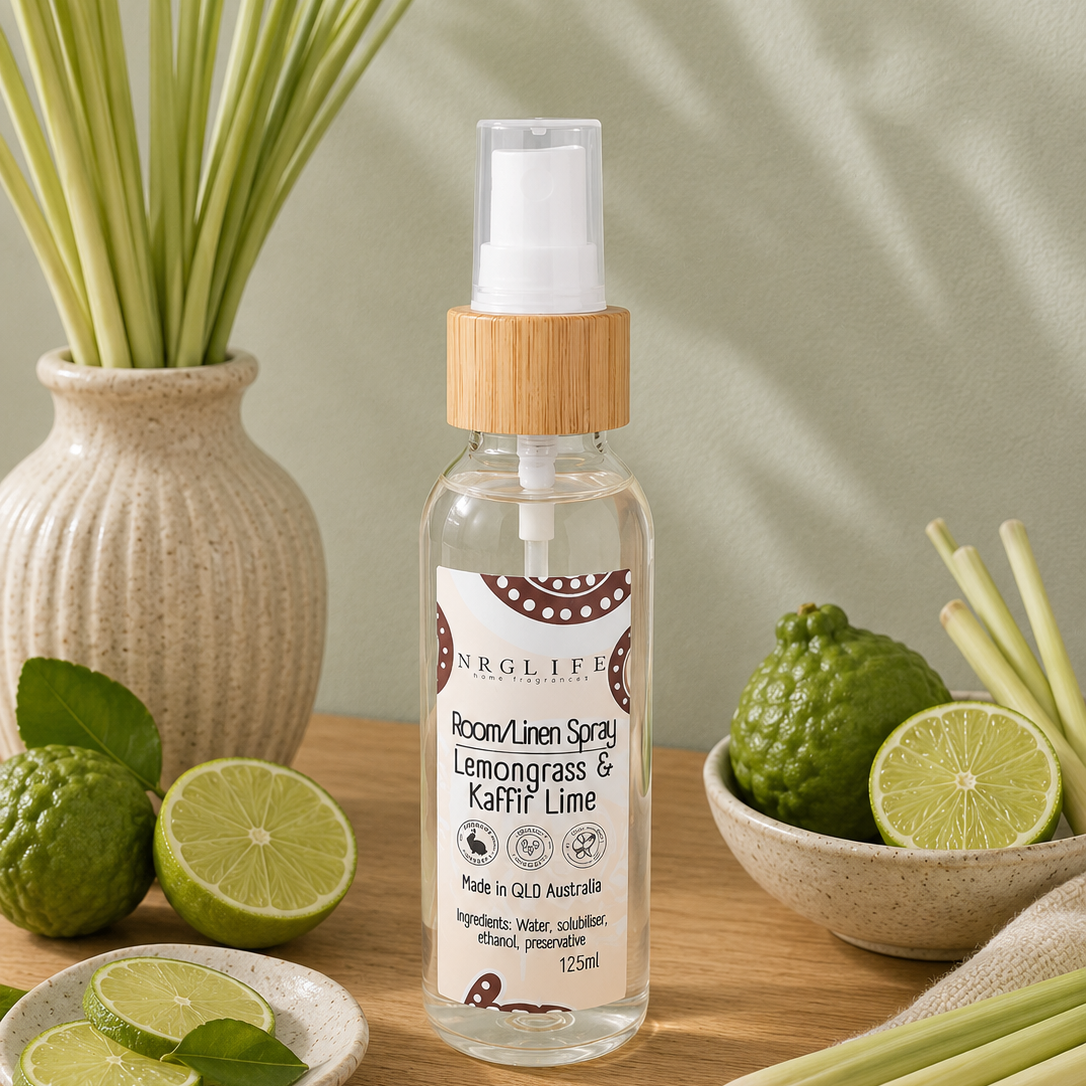 A bottle of Nrglife Icon/Lemongrass and Kaffir Lime Spray centred on a wooden surface, surrounded by lemongrass, kaffir lime, and green leaves in a styled natural setting.
