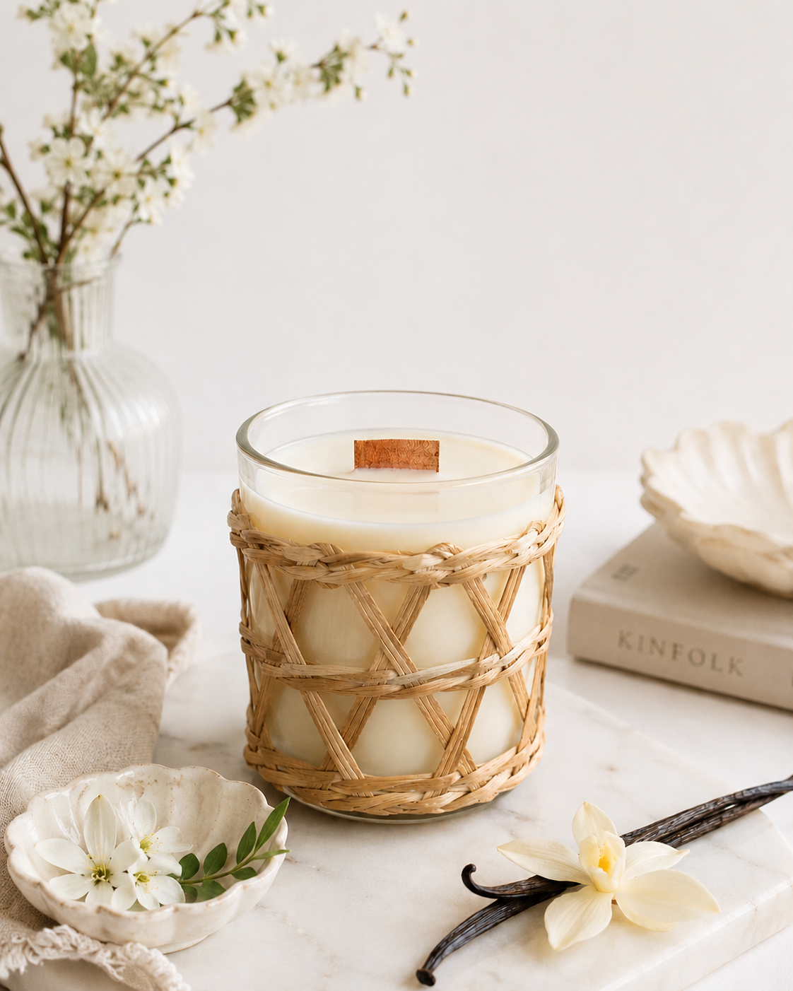 Very Vanilla Candle sitting on a marble table, with a sprig of vanilla and flowers.