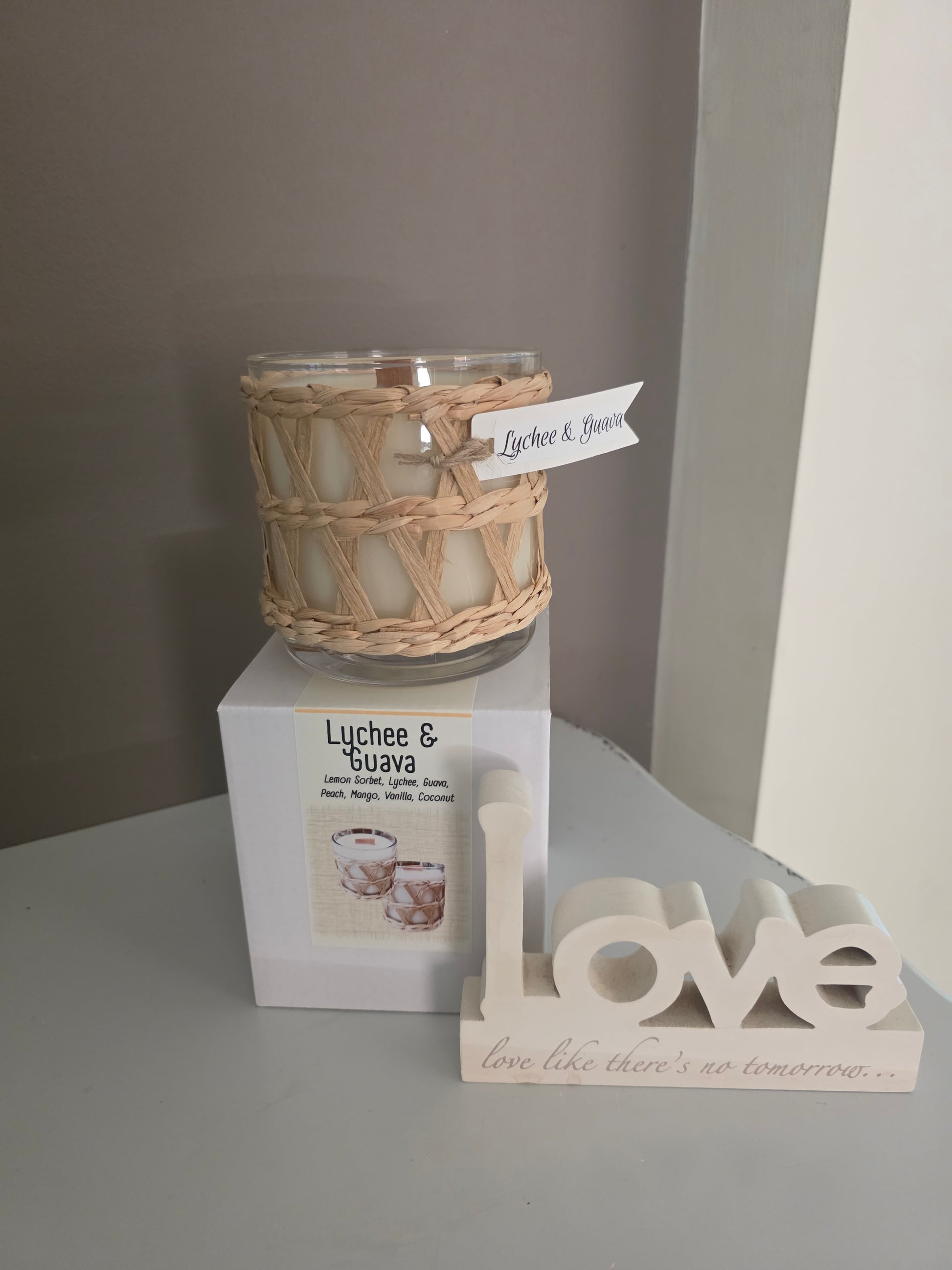 Candle with wicker wrap and 'love' decorative sign on a gray surface
