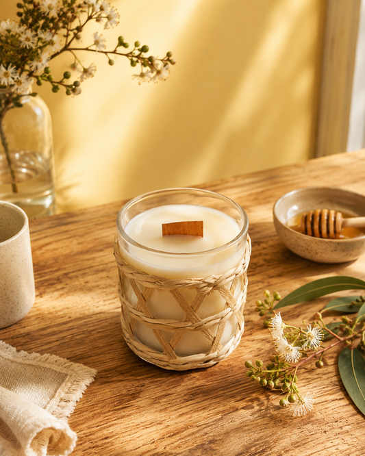 Aussie Honey Blossom fragrance Candle in a textured glass holder on a wooden table with flowers and a bowl in the background