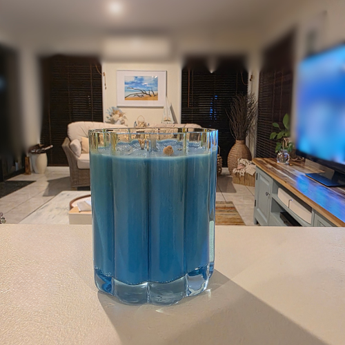 Cloud shaped glass Candle with blue wax on a table with shells and crystal shells on top with a blurred living room background