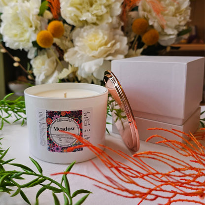 A Large white candle infused with our floral fragrance Meadow, featured with Rose Gold Lid off to the side.