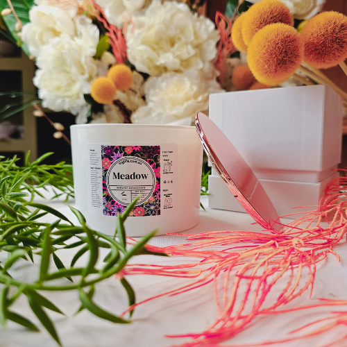 A Large white candle infused with our floral fragrance Meadow, featured with Rose Gold Lid off to the side.