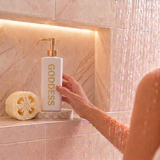 500ml white triangle bottle of Nrglife Goddess Coconut Body Wash sitting in a shower niche.