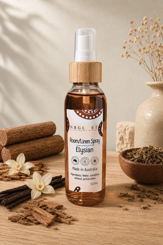 A bottle of Elysian Room/Linen Spray stands on a wooden surface with cinnamon sticks, dried flowers, and a ceramic vase in the background, creating a warm, natural aesthetic.