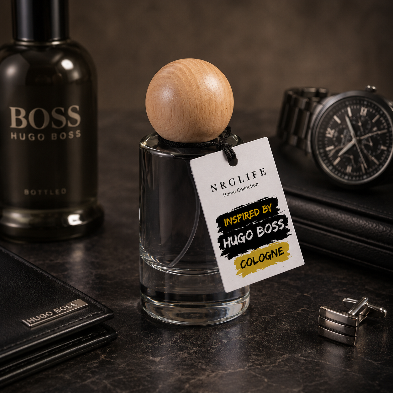 A 25ml Inspired by Hugo Boss cologne bottle with a clear glass body, dark liquid, and a round light wood cap, shown with a hanging white tag reading Nrglife. Other branded items and men's accessories are arranged around it on a dark tabletop.  This is a replicated version not an original.