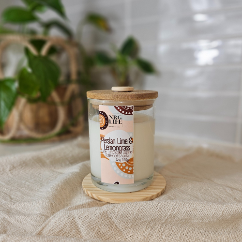 Persian Lime & Lemongrass Signature Candle sitting on a textured surface with a plant in the background. 