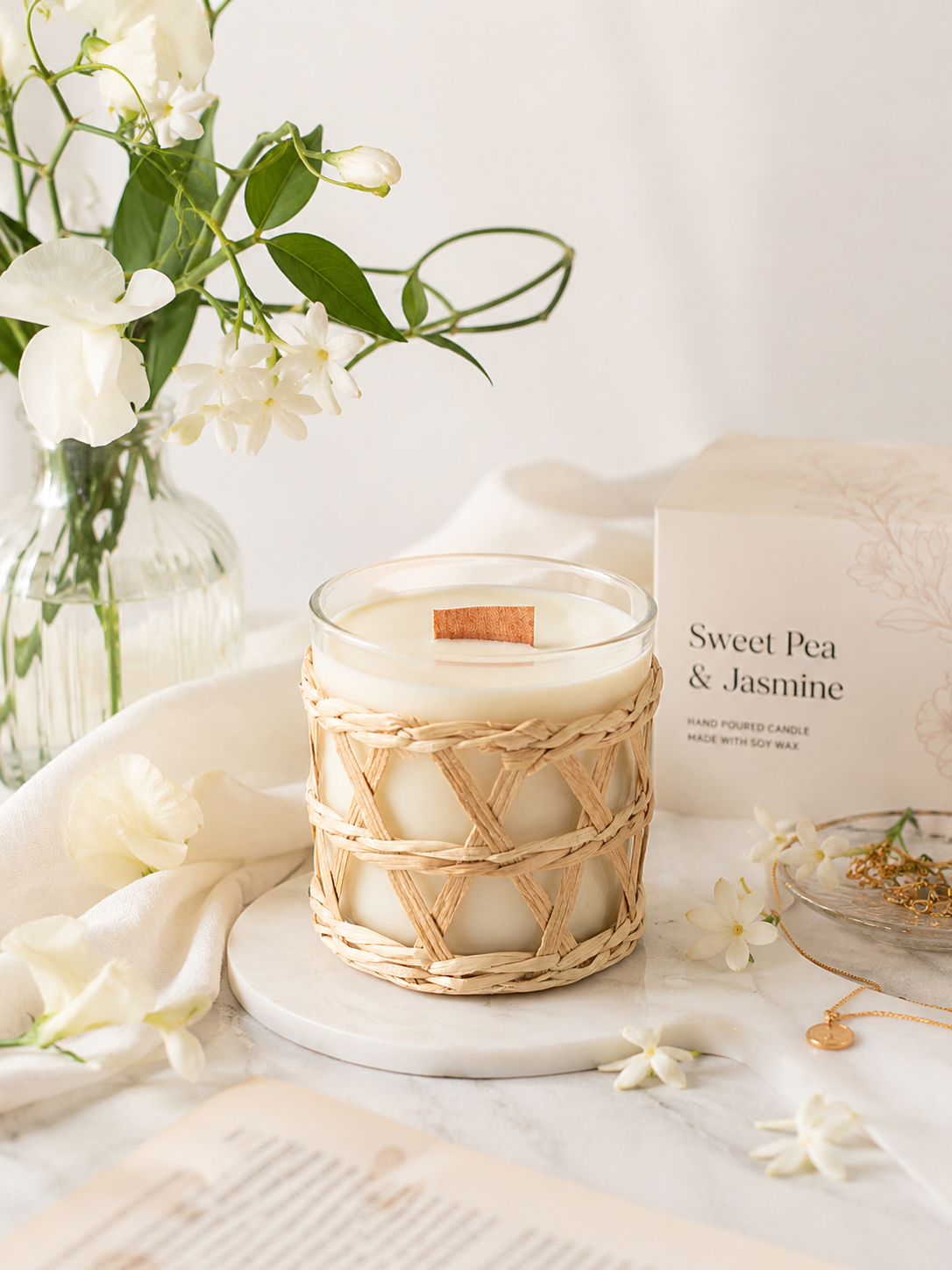A best seller. Beautifully fragrant candle sitting on a table with jasmine flowers surrounding it.