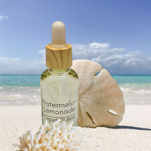 Bottle of 'Watermelon Splash' fragrant diffuser oil blend with a sand dollar on a beach.
