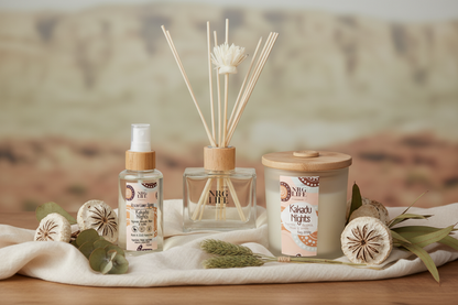 Aromatherapy products including a diffuser, room spray, and a candle in the scent Kakadu Nights on a wooden surface with a blurred natural background.