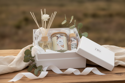 Gift set with candles, diffuser, and room linen spray in a white box on a wooden surface in the crisp scent called Linen.